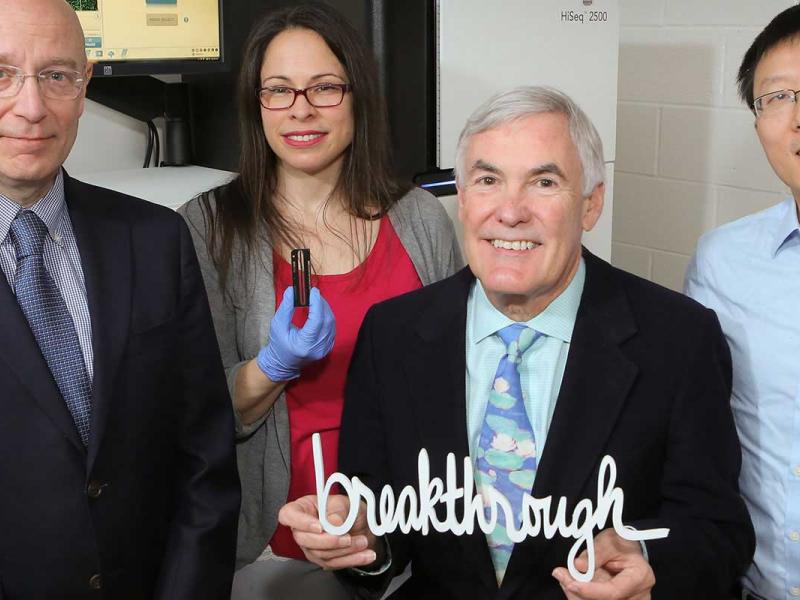 Four people from Penn State Institute for Personalized Medicine stand in a lab One is holding a large 3D-printed version of the word breakthrough.