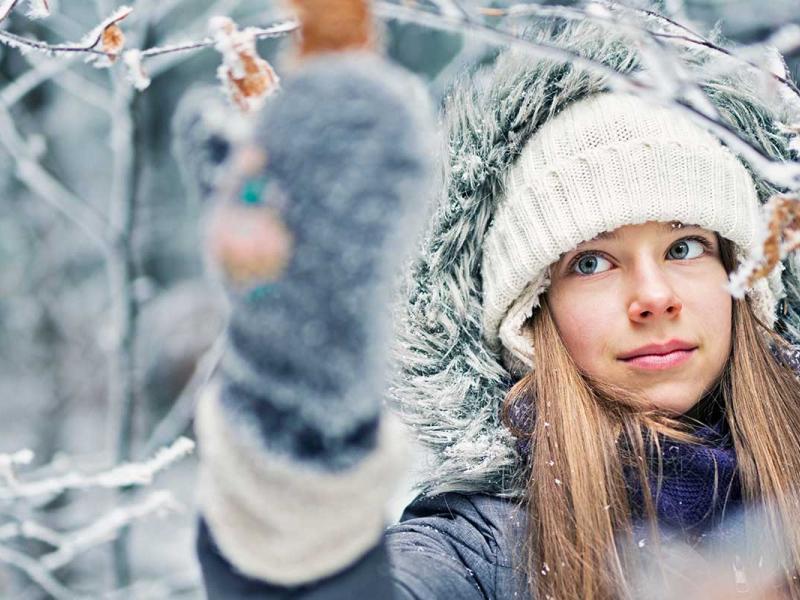 A young girl enjoying beauty of the cold winter morning. The girl is touching tree branches covered with frost.